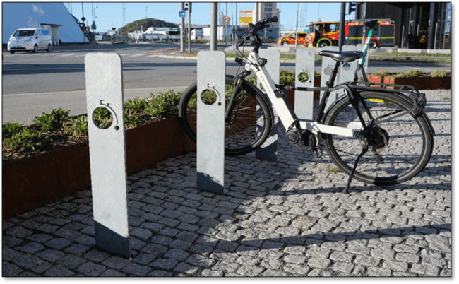 Foto av eksempel p&aring; sykkelparkering som er plassbesparende, men som gir d&aring;rlig st&oslash;tte og f&aring; l&aring;semuligheter. Stativene som er vist p&aring; bildet er flate og rettet oppover, med kun ett gjennomg&aring;ende hull der det er mulighet for &aring; feste sykkell&aring;sen.