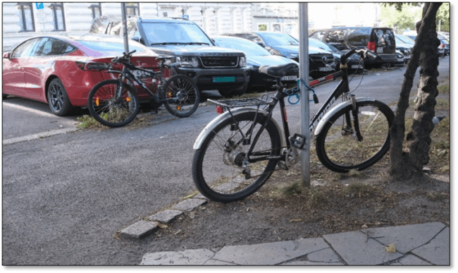 Foto viser to sykler som er l&aring;st fast til hver sin skiltstolpe. Dette er et typisk resultat av manglende tilgjengelig parkering i n&aelig;rheten.