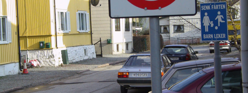 Vei i et boligområde med biler parkert langs veien og et skilt som viser at det er 30 sone, og et skilt som viser at barn leker i området.