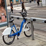 bysykkel parkert ved sykkelstativ ved en vei.