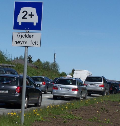 Bilde av biler som står i kø ved et skilt som sier 2+ foran bildet av en bil og kommuniserer at dette gjelder for høyre felt.