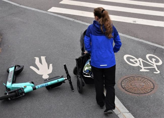 Fotoet viser en kvinne med barnevogn som m&aring; ta en sving rundt en veltet sparkesykkel.