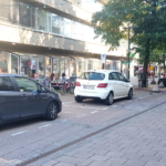 Biler parkert i markerte områder langs en vei i et by/sentrumsmiljø.