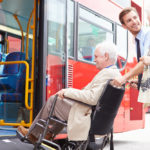 et bilde av en person i rullestol som blir hjelpet inn i en buss.