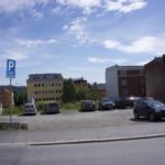 et bilde av biler parkert i en parkeringsplass ved en vei.