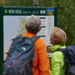 Foto av to syklister som ser på en tavle som inneholder et sykkelkart og stedsinformasjon.