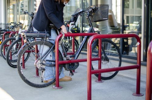 Bildet viser dame som låser ramme og hjul på sykkelen sin fast i et sykkelstativ med kjettinglås
