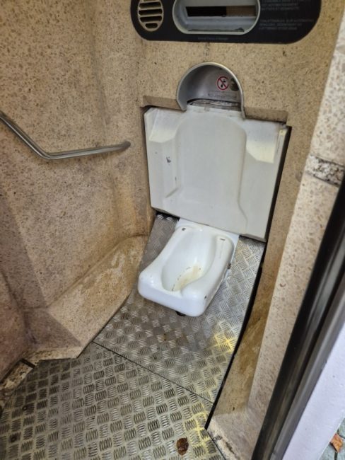 Bildet viser et toalett utenfor Stortinget hvor selve klosettet ikke ser ut som et vanlig klosset. Det har ikke toalett sete, spyleknapp eller vann. Toalettet befinner seg nede p&aring; gulvet, og det er ikke intuitivt hvordan man skal bruke det. Det er heller ingen toalettpapir eller vask.