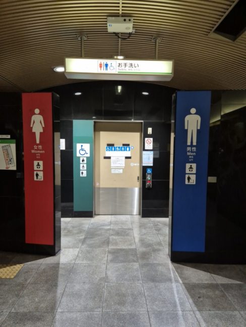 Bildet viser toaletter p&aring; en t-banestasjon i Japan. Skiltene ca. 40x200 cm h&oslash;ye og farget i r&oslash;dt (dame) og bl&aring;tt (herre) og turkis (HC) slik at det er sv&aelig;rt lett &aring; f&aring; &oslash;ye p&aring; dem ogs&aring; fra avstand.