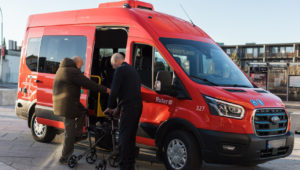 Fotoet viser en minibuss fra Ruter, der en eldre mann hjelpes ombord i bussen.