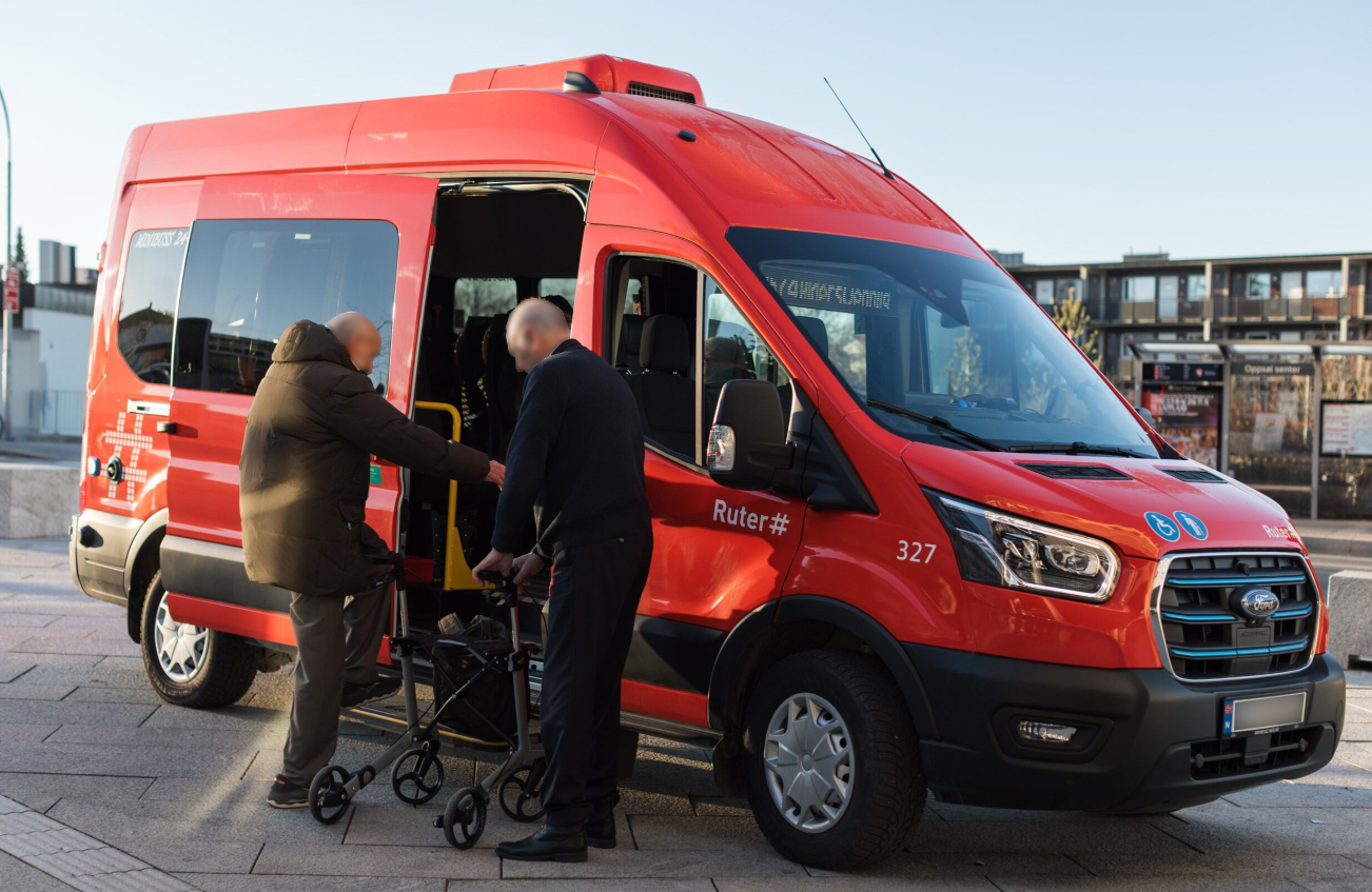 Fotoet viser en minibuss fra Ruter, der en eldre mann hjelpes ombord i bussen.