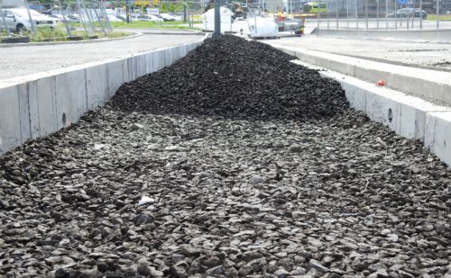 : Fotoet viser en betongfordypning ved siden av en vei. Fordypningen blir fylt med masse (biokull, pukk mm).