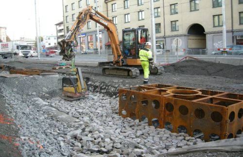 Fotoet viser en kranbil som l&oslash;fter p&aring; plass st&oslash;pejernskummer ved siden av veien.